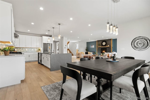 dining area featuring stairs, recessed lighting, a fireplace, and light wood-type flooring