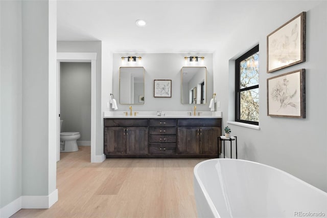 bathroom with wood finished floors, a freestanding tub, toilet, and a sink