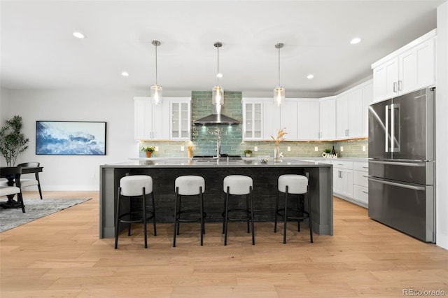 kitchen featuring wall chimney range hood, a center island with sink, a kitchen bar, light wood-type flooring, and stainless steel appliances