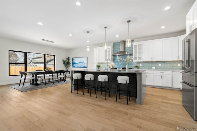 kitchen with a breakfast bar, wall chimney range hood, high quality fridge, light wood-type flooring, and backsplash