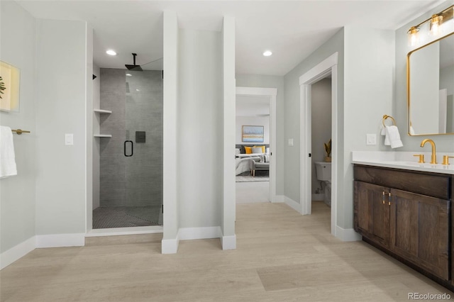 ensuite bathroom with a stall shower, wood finished floors, recessed lighting, baseboards, and vanity