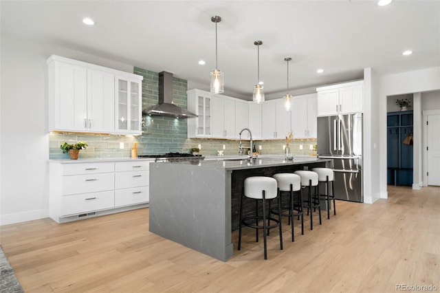 kitchen featuring wall chimney range hood, high end fridge, a sink, and light wood-style floors