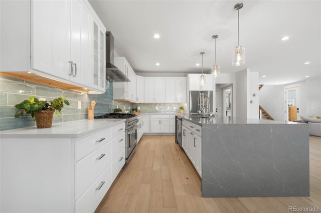 kitchen featuring wall chimney range hood, decorative backsplash, stainless steel appliances, light wood finished floors, and white cabinets