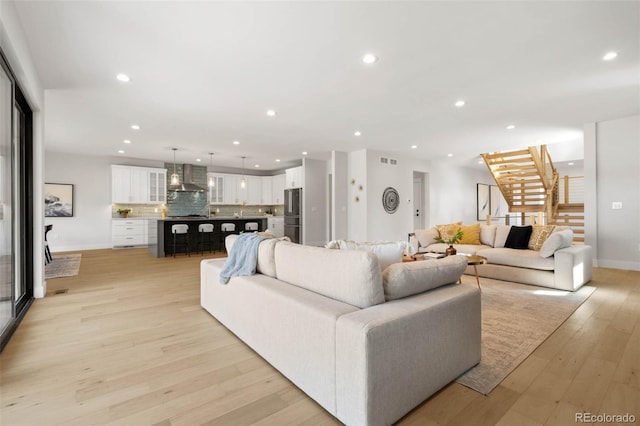 living area with light wood finished floors, baseboards, recessed lighting, visible vents, and stairs
