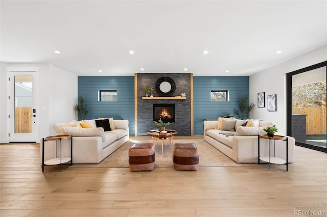 living room with light wood finished floors, an accent wall, a large fireplace, and recessed lighting
