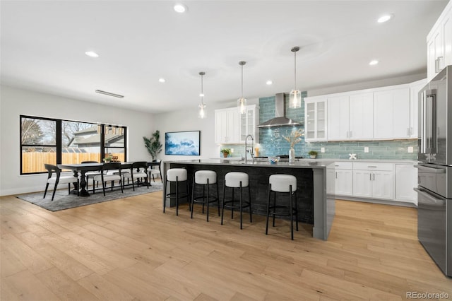 kitchen with a breakfast bar, wall chimney range hood, decorative backsplash, and high end refrigerator