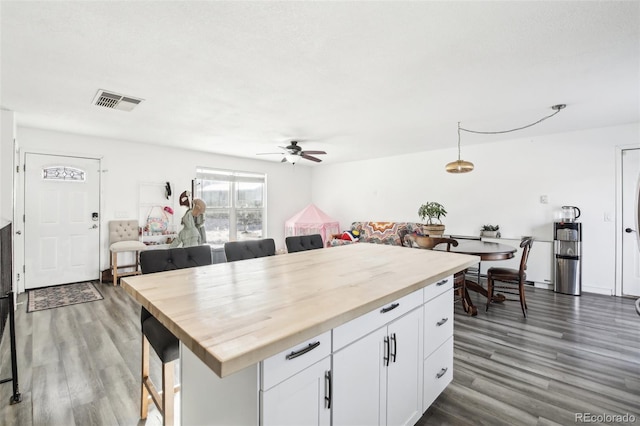 kitchen featuring ceiling fan, butcher block counters, white cabinetry, dark hardwood / wood-style floors, and a kitchen bar