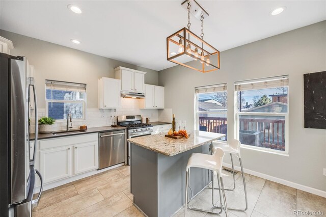 kitchen with tasteful backsplash, white cabinets, appliances with stainless steel finishes, under cabinet range hood, and a sink