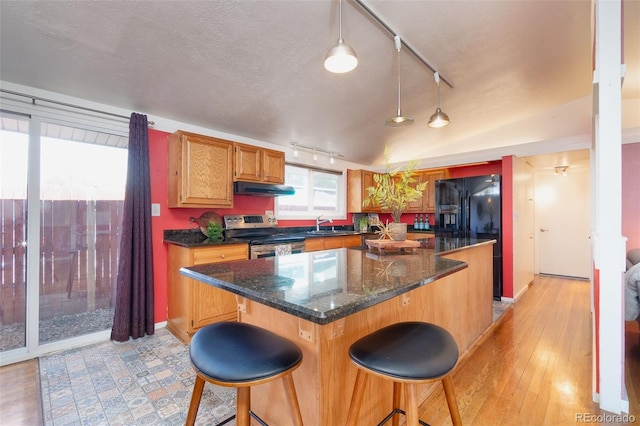 kitchen featuring under cabinet range hood, electric range, a kitchen island, vaulted ceiling, and a kitchen bar