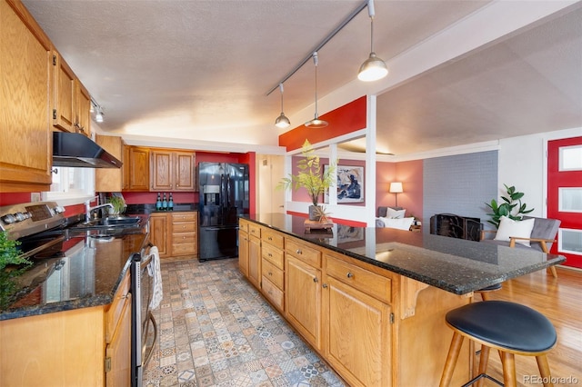 kitchen featuring a brick fireplace, a kitchen island, under cabinet range hood, a kitchen bar, and black fridge