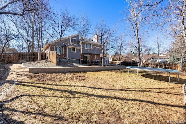 back of house with a trampoline, a fenced backyard, brick siding, and a chimney