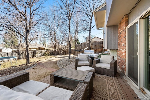 wooden deck with a trampoline, outdoor lounge area, a fenced backyard, a grill, and a patio