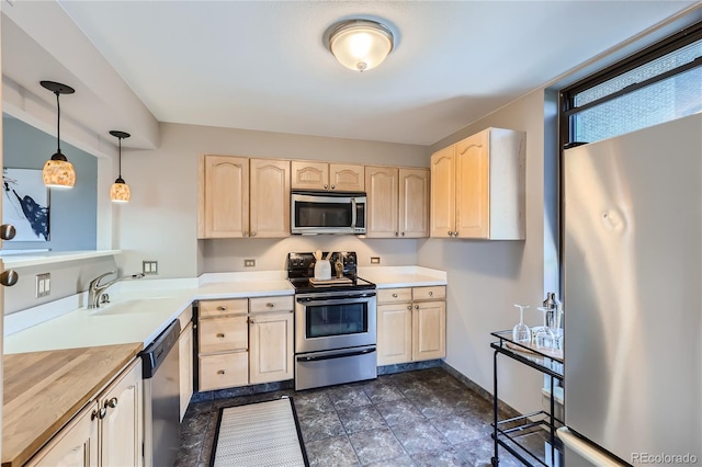 kitchen featuring dark tile patterned flooring, appliances with stainless steel finishes, hanging light fixtures, light brown cabinetry, and sink