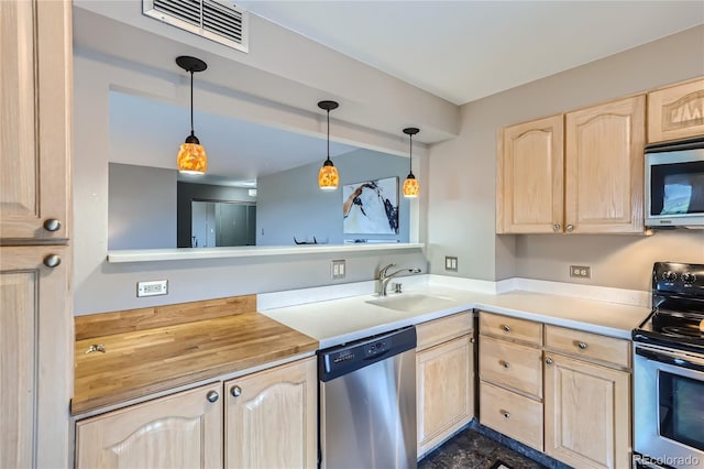 kitchen with stainless steel appliances, light brown cabinetry, hanging light fixtures, dark tile patterned flooring, and sink