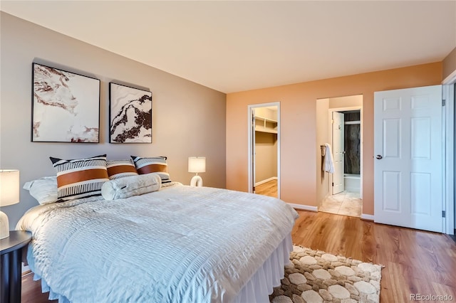 bedroom with a closet, a spacious closet, light wood-style floors, connected bathroom, and baseboards