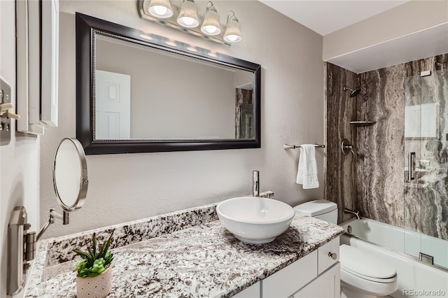 bathroom with a textured wall, bath / shower combo with glass door, vanity, and toilet