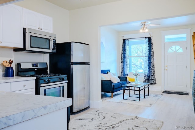 kitchen featuring a ceiling fan, light wood-style flooring, stainless steel appliances, baseboards, and white cabinets