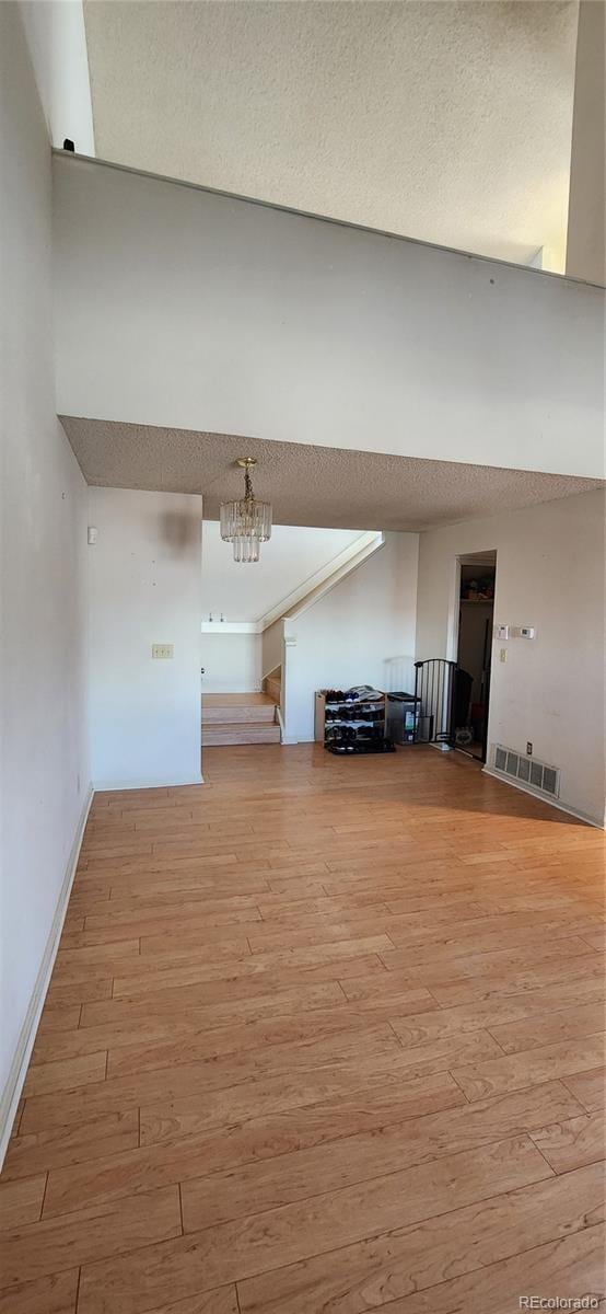 unfurnished living room with light wood-style floors, a textured ceiling, visible vents, and a notable chandelier