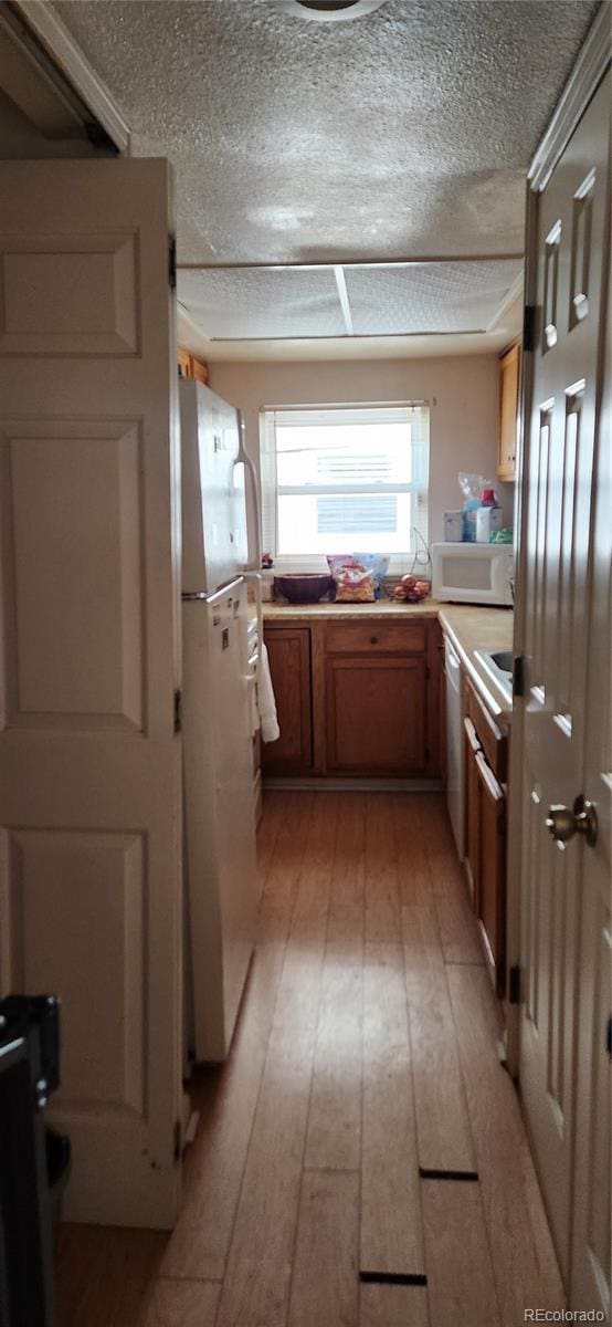 kitchen with white appliances, light wood finished floors, brown cabinets, light countertops, and a textured ceiling