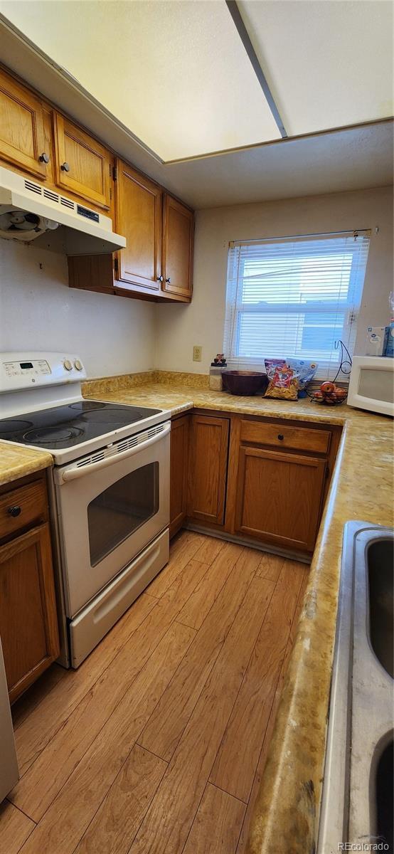 kitchen with brown cabinets, light wood finished floors, light countertops, white appliances, and under cabinet range hood