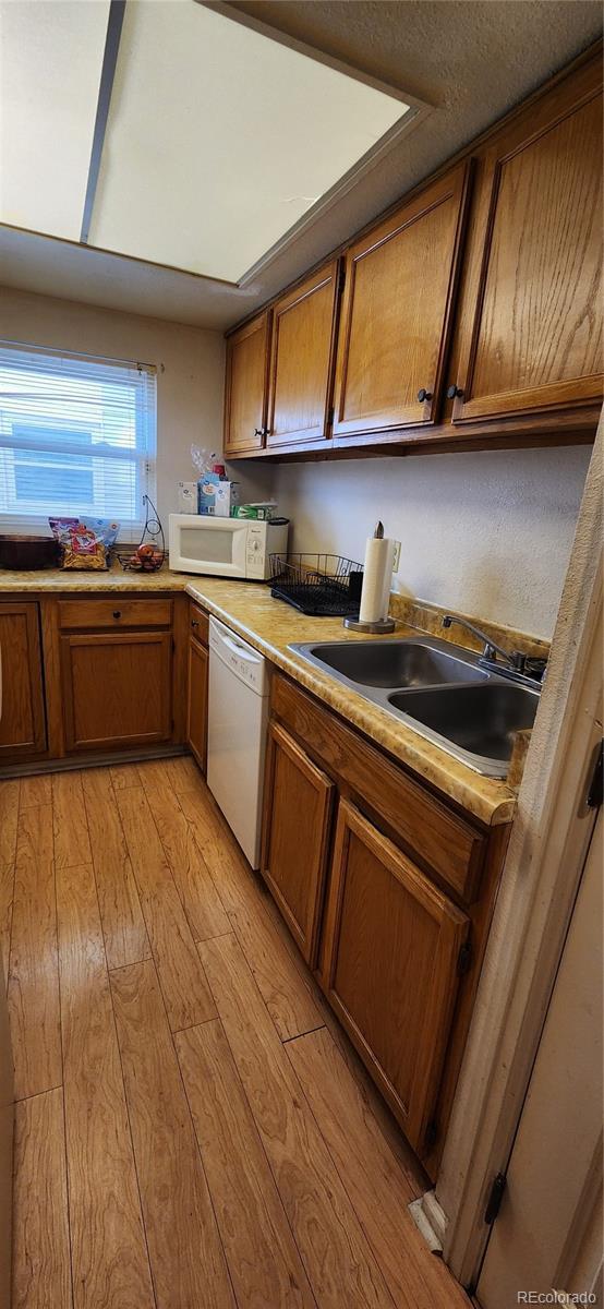 kitchen featuring brown cabinets, light countertops, a sink, light wood-type flooring, and white appliances