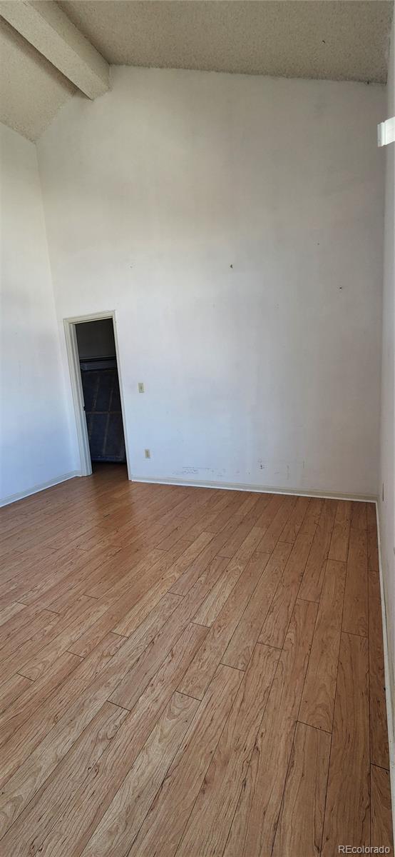 spare room featuring light wood-style floors, vaulted ceiling with beams, and a textured ceiling