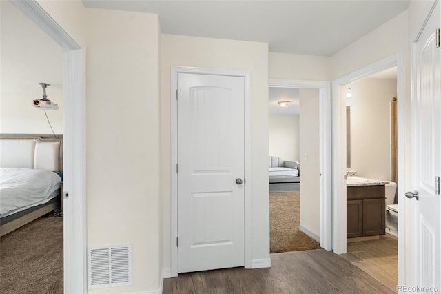 hallway featuring dark wood-type flooring, visible vents, dark carpet, and baseboards