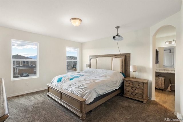 carpeted bedroom featuring baseboards, visible vents, arched walkways, and ensuite bathroom