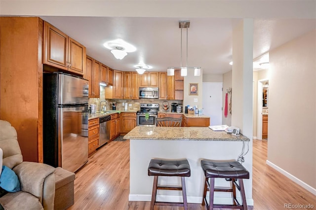 kitchen with backsplash, light stone counters, stainless steel appliances, light hardwood / wood-style flooring, and hanging light fixtures