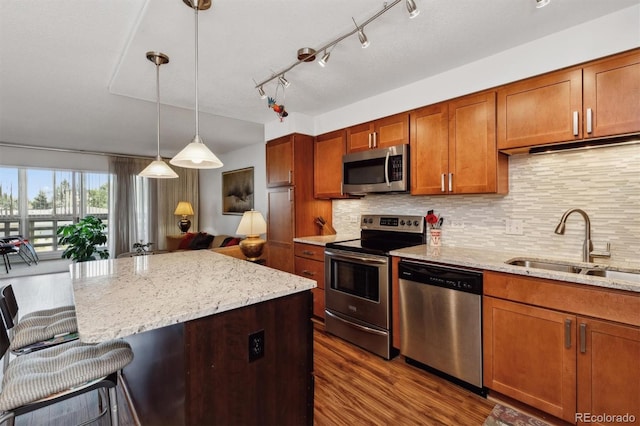 kitchen with light stone countertops, appliances with stainless steel finishes, sink, hanging light fixtures, and dark wood-type flooring