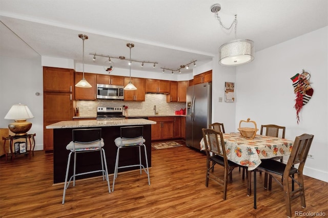 kitchen with dark wood finished floors, a kitchen island, decorative backsplash, hanging light fixtures, and appliances with stainless steel finishes