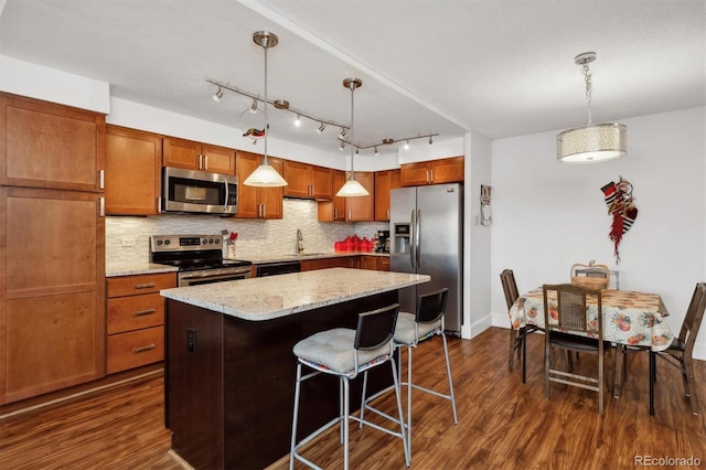 kitchen with stainless steel appliances, dark wood-style floors, a sink, decorative backsplash, and a kitchen island