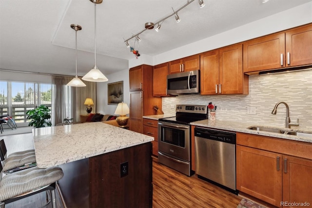 kitchen featuring dark wood finished floors, light stone counters, stainless steel appliances, a sink, and a breakfast bar area