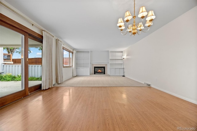 7483 W Cedar Cir, Lakewood, CO 80226 - unfurnished living room with wood finished floors, built in shelves, a chandelier, baseboards, and a glass covered fireplace