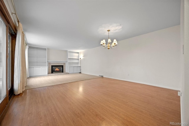 7483 W Cedar Cir, Lakewood, CO 80226 - unfurnished living room with a tiled fireplace, a chandelier, wood finished floors, built in shelves, and baseboards