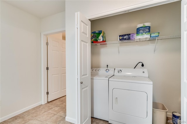 washroom featuring washing machine and dryer, laundry area, baseboards, and light tile patterned floors