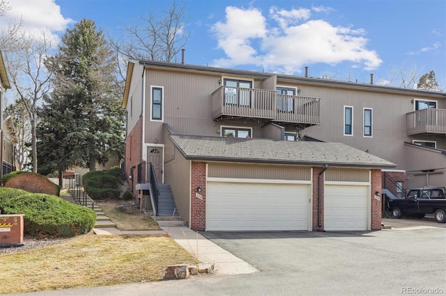 view of property featuring brick siding, a balcony, aphalt driveway, and a garage