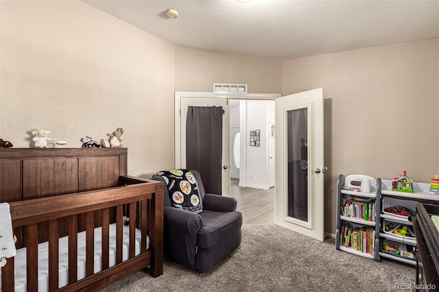 carpeted bedroom featuring a nursery area and a textured ceiling