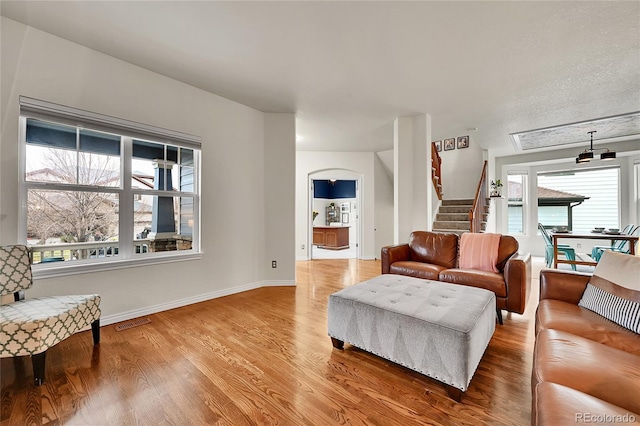 living room featuring stairway, baseboards, light wood-type flooring, and visible vents