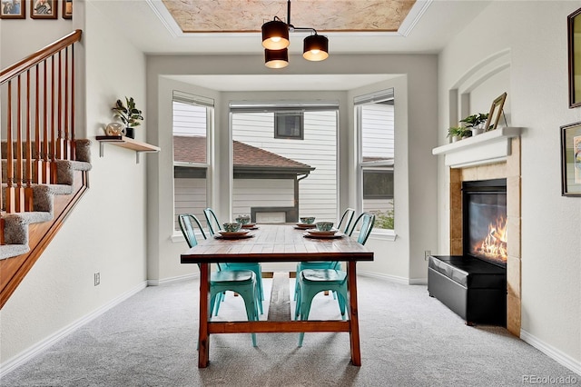 carpeted dining space with stairway, baseboards, a tile fireplace, and a raised ceiling