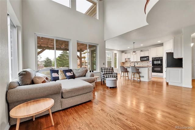 living area with a towering ceiling, visible vents, baseboards, light wood finished floors, and recessed lighting