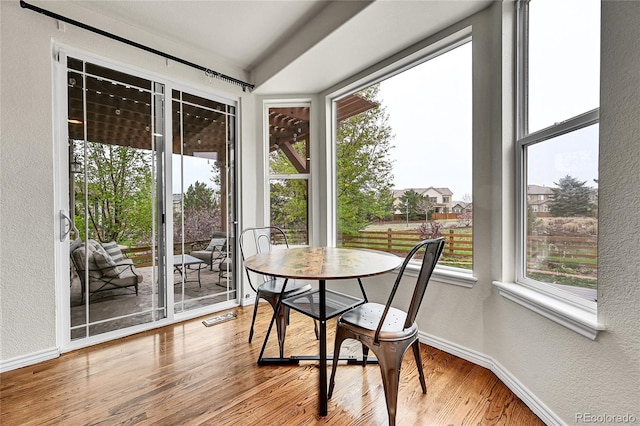 sunroom featuring baseboards, a textured wall, and wood finished floors