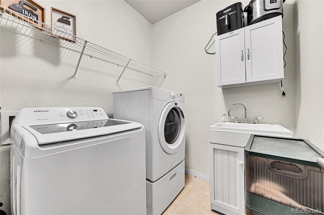 laundry area with cabinet space, a sink, baseboards, light tile patterned floors, and washer and clothes dryer