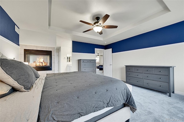 bedroom with a fireplace, baseboards, ceiling fan, a tray ceiling, and carpet