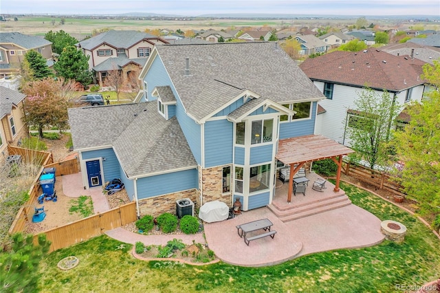 back of property featuring a residential view, a patio area, a fenced backyard, a shingled roof, and stone siding