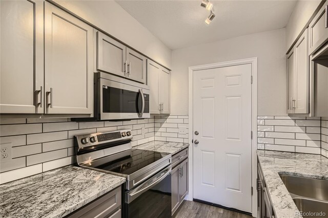 3401 W Milan Ave, Denver, CO 80236 - kitchen featuring appliances with stainless steel finishes, dark wood finished floors, light stone countertops, tasteful backsplash, and gray cabinetry