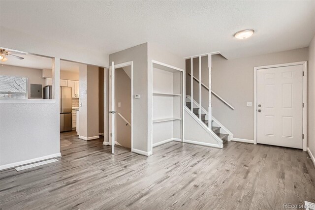 3401 W Milan Ave, Denver, CO 80236 - unfurnished living room with light wood-style floors, ceiling fan, stairs, baseboards, and a textured ceiling