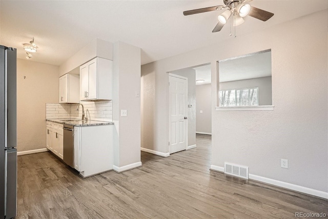 3401 W Milan Ave, Denver, CO 80236 - kitchen featuring a sink, stainless steel appliances, backsplash, white cabinetry, and wood finished floors