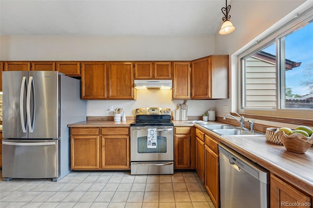 kitchen featuring light countertops, under cabinet range hood, brown cabinets, a sink, and appliances with stainless steel finishes