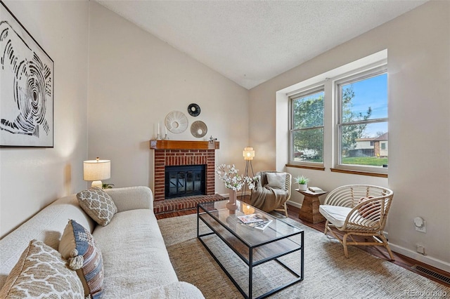 living area featuring visible vents, a fireplace, vaulted ceiling, wood finished floors, and baseboards